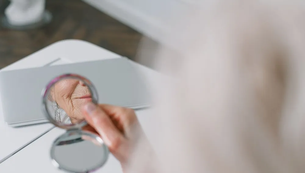 tanda penuaan dini paling cepat di usia muda - wanita Indonesia bercermin khawatir dan memegang wajah cek kerutan halus dan flek hitam